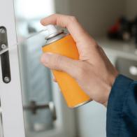 closeup of a caucasian man, in blue overalls, spraying some lubricating oil on the hinge of a white door, in a panoramic format to use as web banner or header